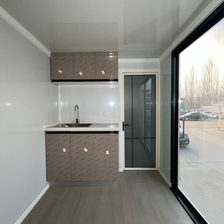Modern kitchenette with gray textured cabinetry, sink, and stovetop beside a large glass door overlooking a parking lot